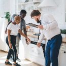 Confident estate agent showing kitchen to African American thoughtful couple Professional bearded chubby man in formal outfit with clipboard inspecting oven together with attentive ethnic couple while standing at modern sunny apartment